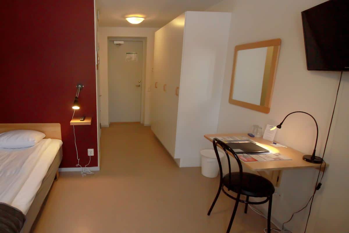 A hotel room with a bed, desk, chair, and a television.