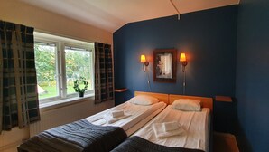 A hotel room with two beds, a window with curtains, a wall-mounted lamp, and a framed picture. - Nipanhotellet (Solleftea)