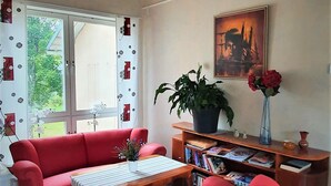A living room with a red sofa, a wooden coffee table, and a red armchair. There is a bookshelf with books and a potted plant. - Nipanhotellet (Solleftea)