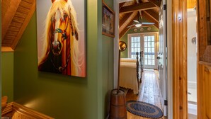 Un couloir avec un plafond en bois, un tableau représentant un cheval accroché au mur et une porte donnant sur une pièce où se trouve une baignoire.