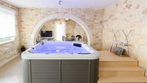 Ein Wellnessraum mit Whirlpool, Steinwänden, Kamin und Fernseher.