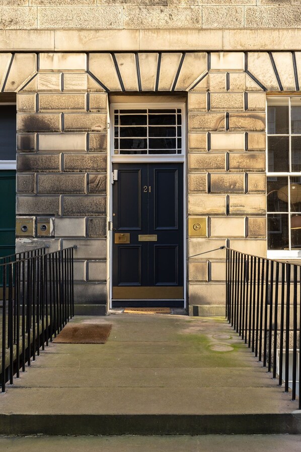 A building entrance with a black door marked "21", a metal gate, and a stone wall.