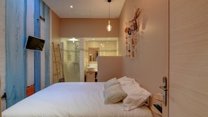 Een slaapkamer met een bed, een aan de muur bevestigde televisie en een badkamer zichtbaar door een geopende deur.