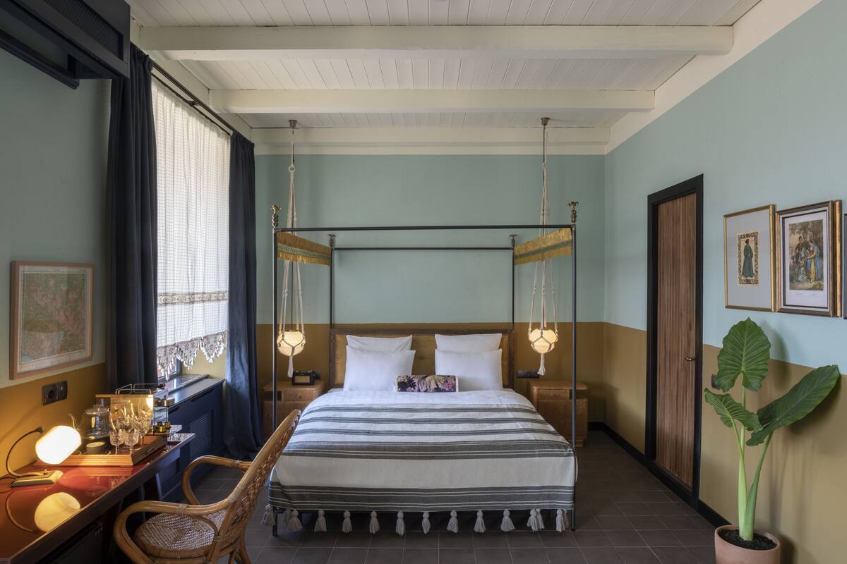 A bedroom with a four-poster bed, bedside tables, a desk with a lamp, and a large potted plant.