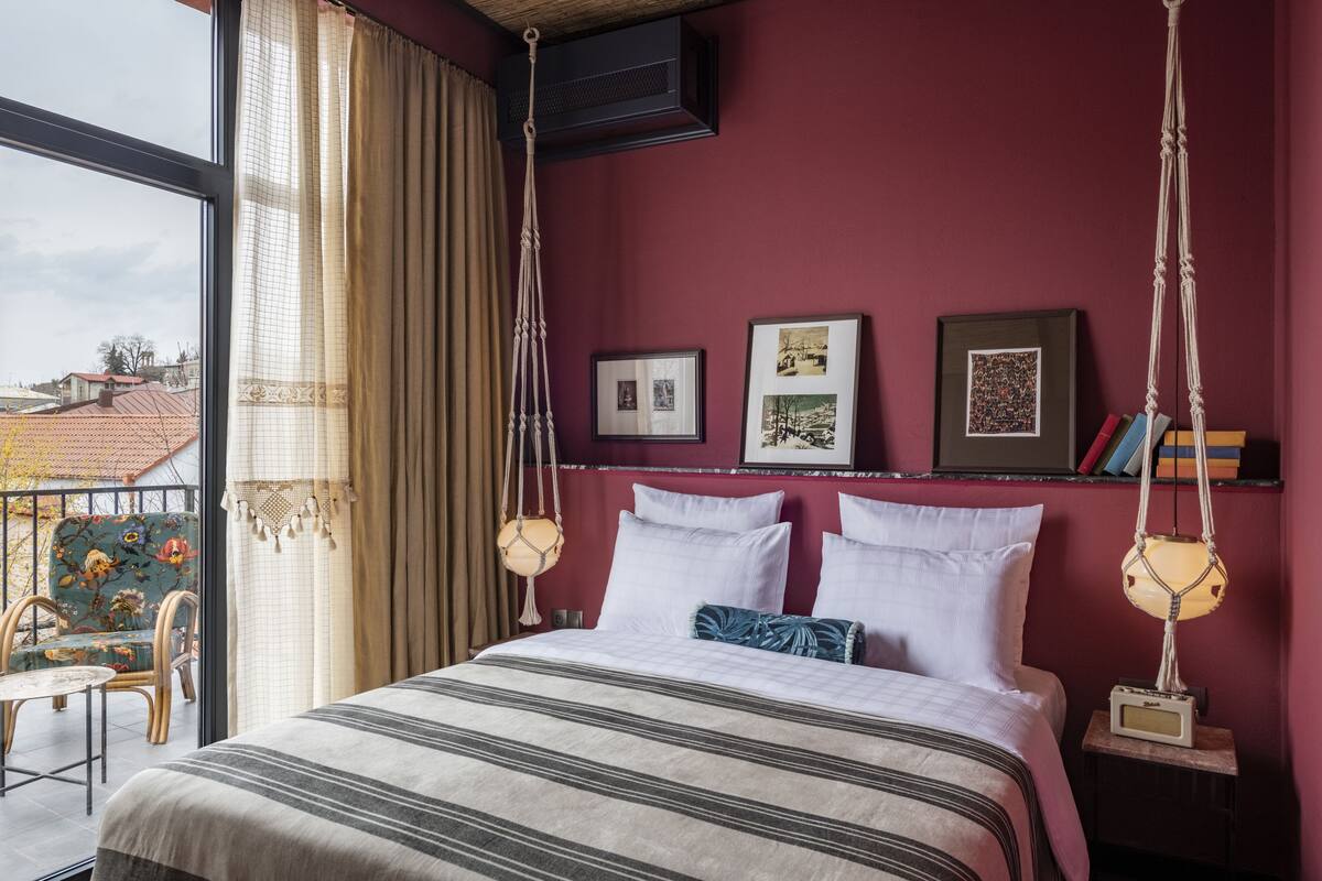 A bedroom with a large bed, a hanging macrame light, and framed pictures on the wall.