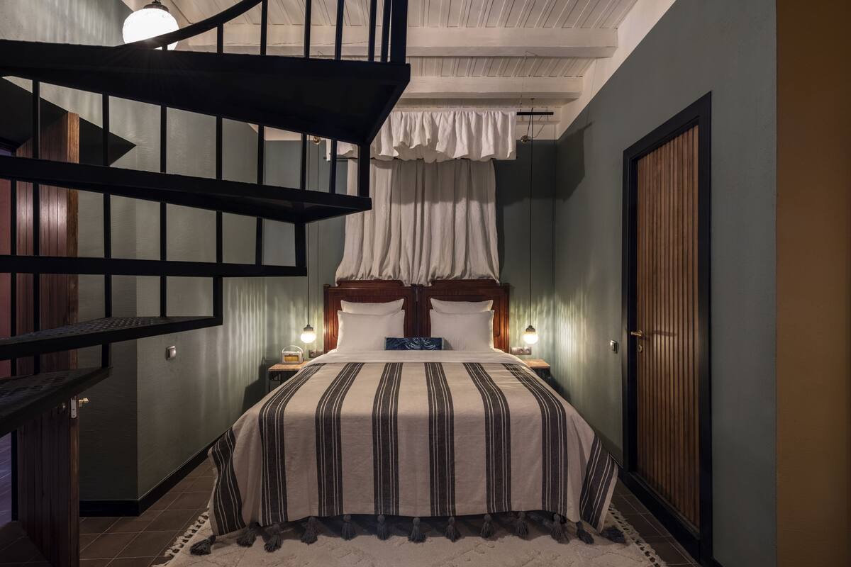 A bedroom with a bed, a nightstand, a wooden door, and a staircase.