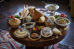 A round wooden table with various food items and utensils, including cheese, bread, and vegetables.