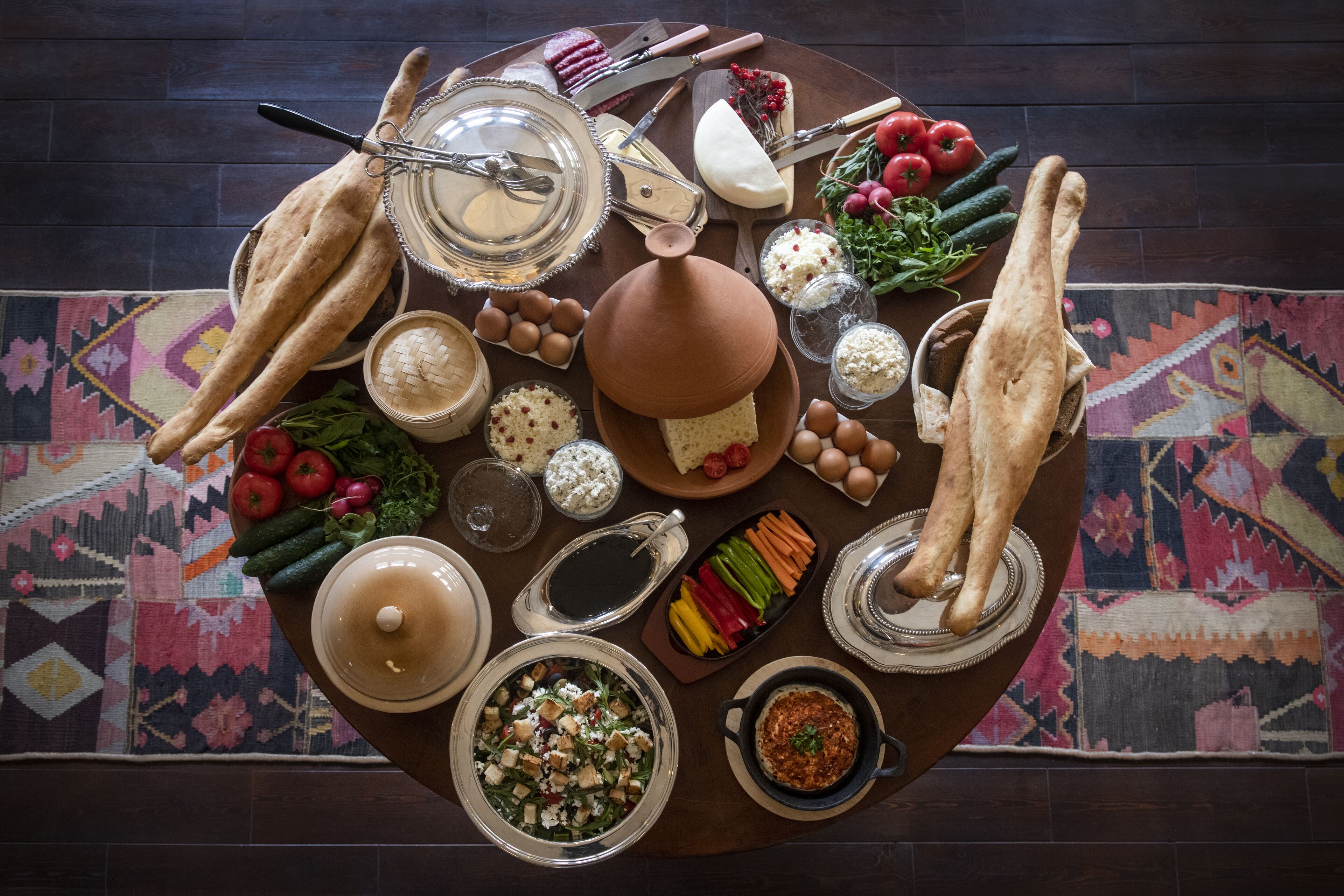 Una mesa redonda con diversos alimentos y utensilios, como pan, queso, verduras y condimentos.