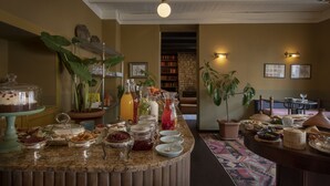 Un bufé de desayuno con diversas opciones de comida y bebidas, una estantería y plantas en macetas.