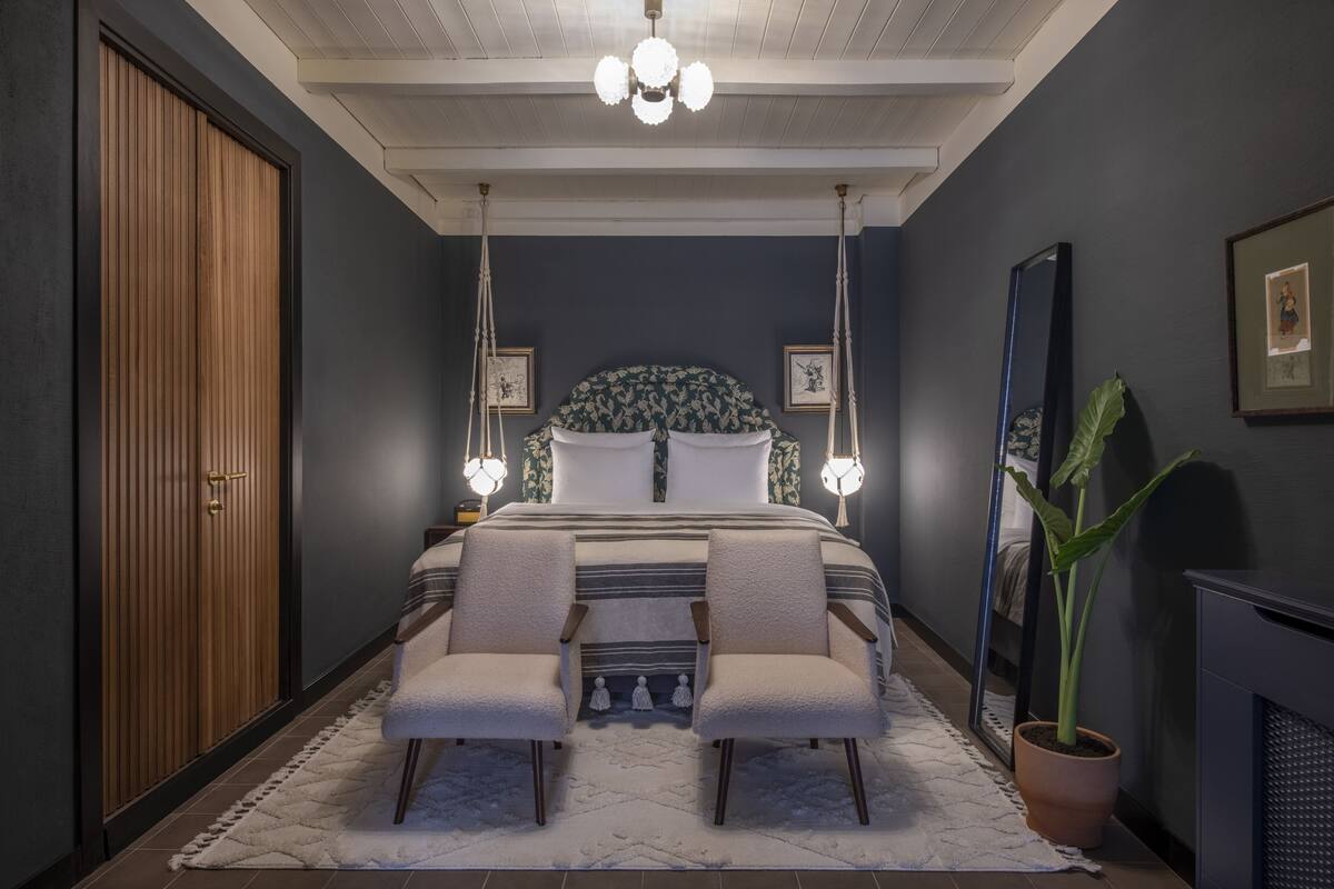 A bedroom with a bed, two chairs, a large mirror, and a potted plant.