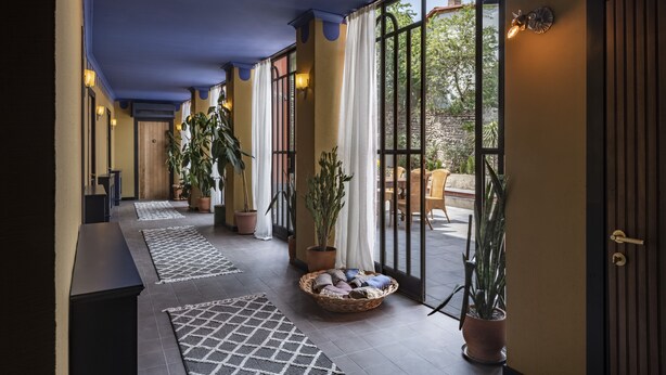 Un pasillo con plantas en macetas, una cesta con ropa y vista a un área exterior.