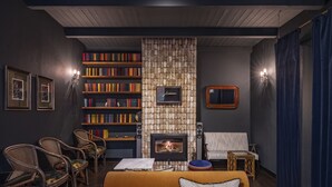 Una sala de estar acogedora con chimenea, estanterías, muebles de mimbre y una cortina azul.