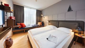 A hotel room with two beds, a desk, a chair, a window with curtains, and a wall-mounted shelf.