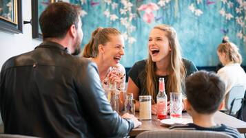 Eine Gruppe von Personen sitzt an einem Tisch in einem Restaurant mit Blumenmuster-Tapete und gerahmten Bildern an der Wand.