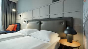 A hotel room with a large bed, a bedside table, a lamp, and a view of the city through the window.