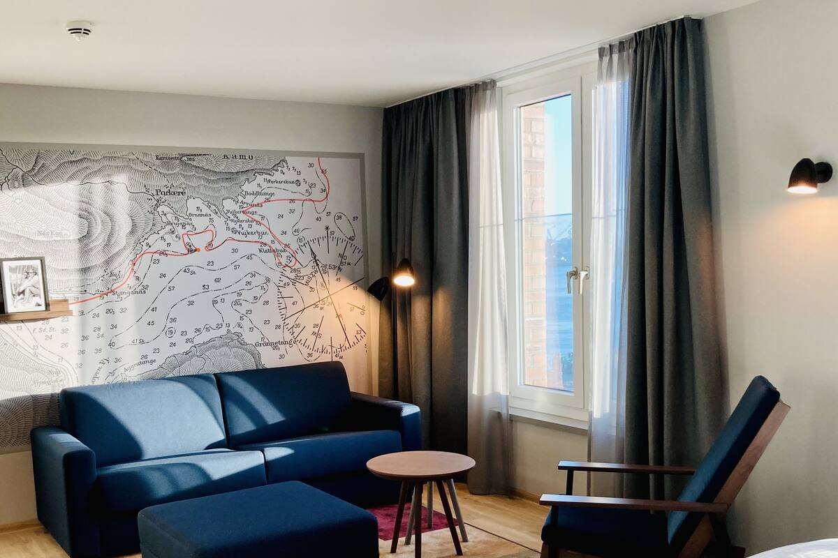 Ein modernes Hotelzimmer mit einem blauen Sofa, einem kleinen runden Tisch, einem Holzstuhl und einem Bett.