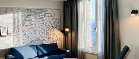 Una habitación de hotel moderna con un sofá azul, una pequeña mesa redonda, una silla de madera y una cama.