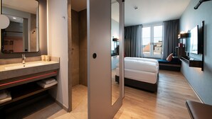 Ein modernes Hotelzimmer mit einem großen Spiegel, einem Bett, einem Fernseher und Blick ins Freie.