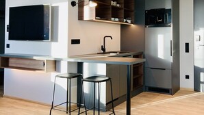 A modern kitchen with a built-in microwave, a large island with bar stools, and a flat-screen TV mounted on the wall. - unique by ATLANTIC Hotels Kiel (Kiel)