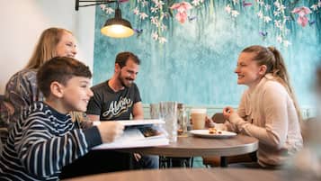 Una familia comiendo en una mesa con un mural floral, una lámpara y una jarra de vidrio.