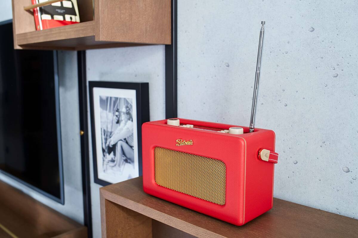 Ein rotes, altes Radio auf einem Holztisch vor einer Betonwand mit gerahmten Bildern.