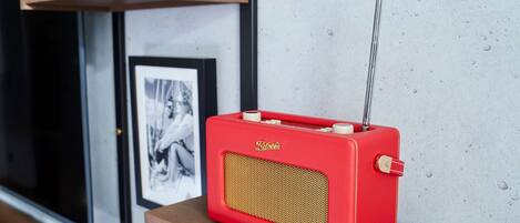 Una radio vintage rossa su un tavolo di legno, con cornici appese a una parete in cemento.