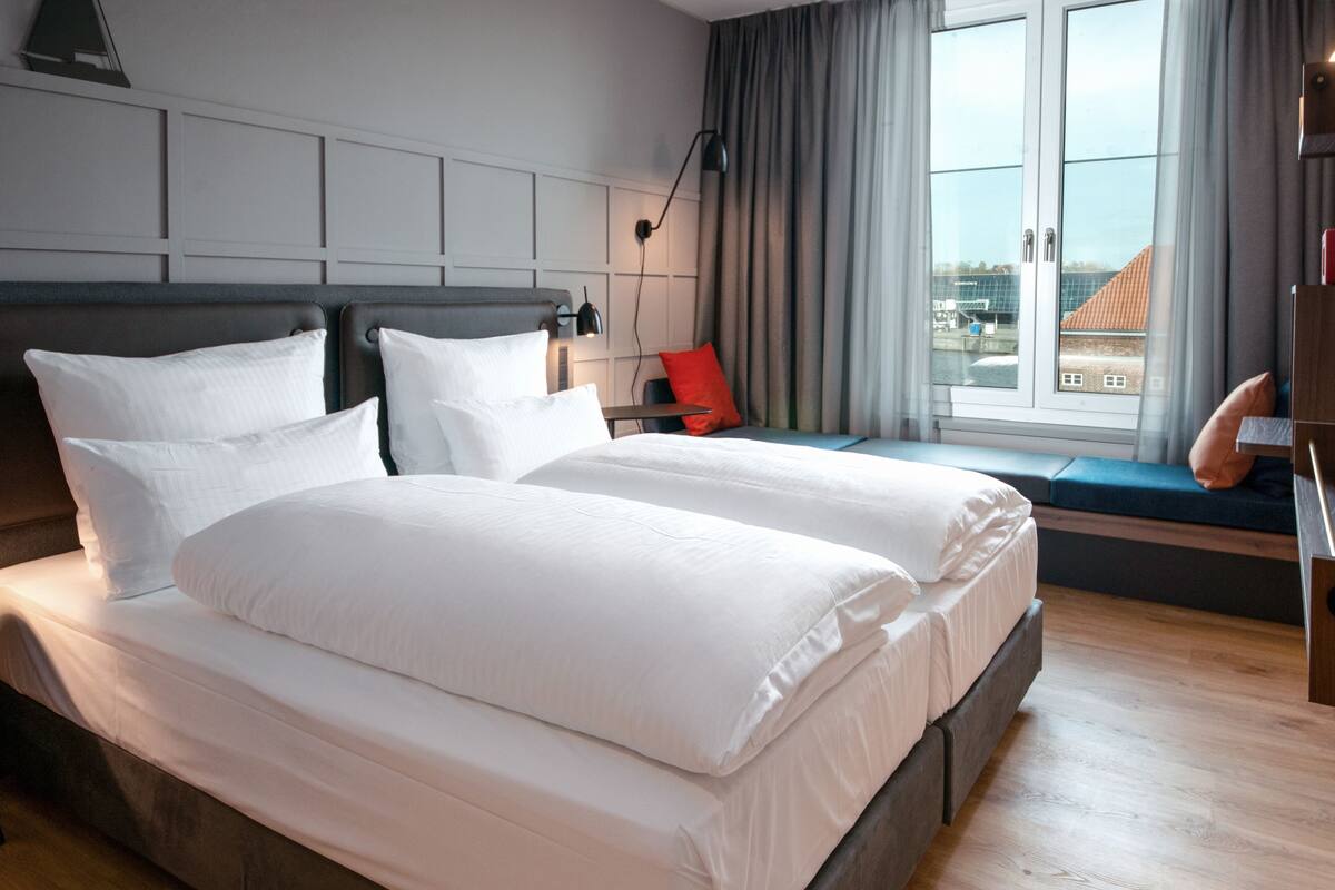Ein Hotelzimmer mit einem großen Bett, einer Sitzecke am Fenster und Blick auf Gebäude.