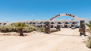 Der Eingang eines Resorts mit einem Schild, das "Paradise Villas" zeigt, und ein modernes Gebäude mit mehreren Balkonen.