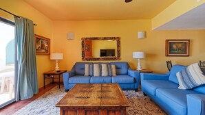 Ein Wohnzimmer mit einem blauen Sofa, zwei Beistelltischen mit Lampen, einem Holztisch als Couchtisch und einem großen Spiegel an der Wand.
