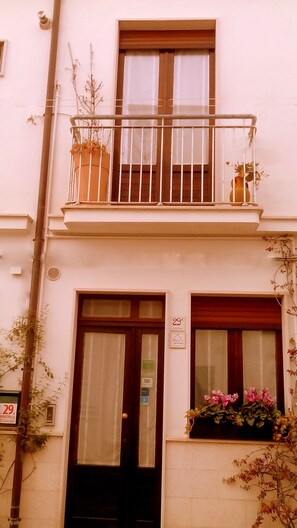 A two-story building with a balcony, a door, and a window with a flower box.