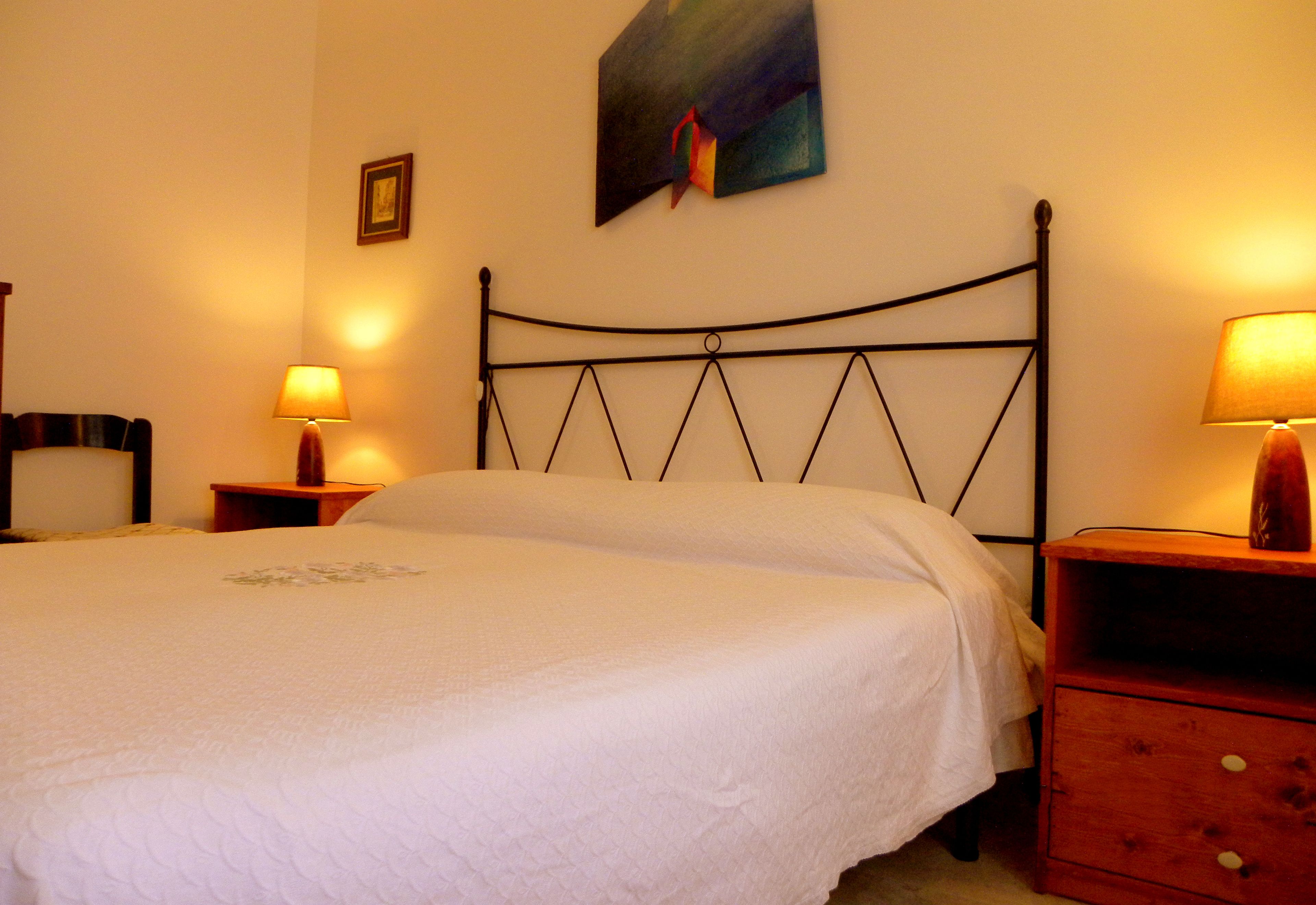Een slaapkamer met een bed, twee nachtkastjes met lampen, een hoofdeinde en een schilderij aan de muur.