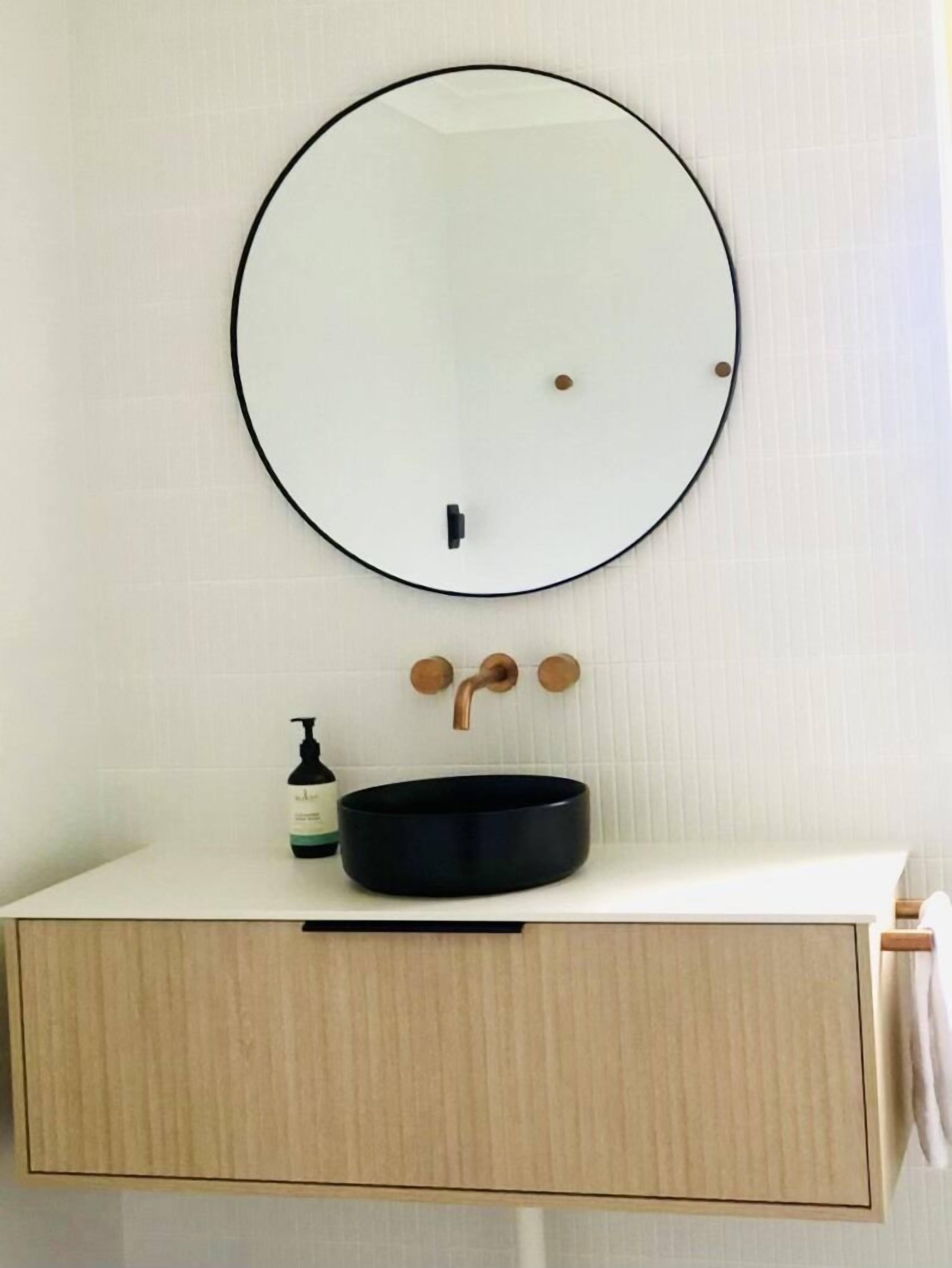Un bagno con uno specchio rotondo, un lavandino nero e una bottiglia di sapone.