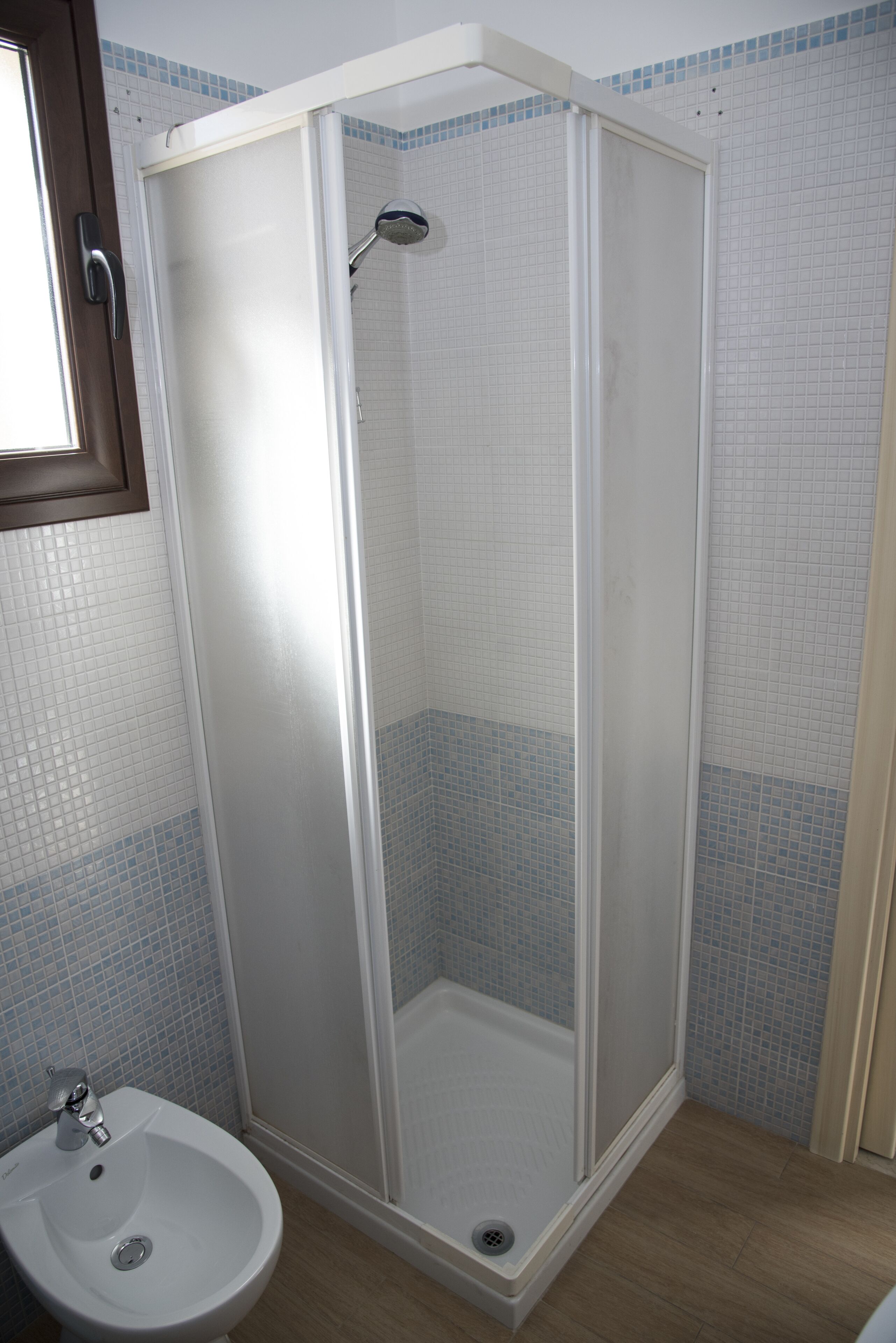 Un box de ducha con puerta de cristal, un lavabo y paredes con azulejos.