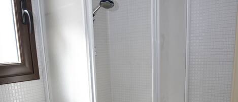 Un box de ducha con puerta de cristal, un lavabo y paredes con azulejos.