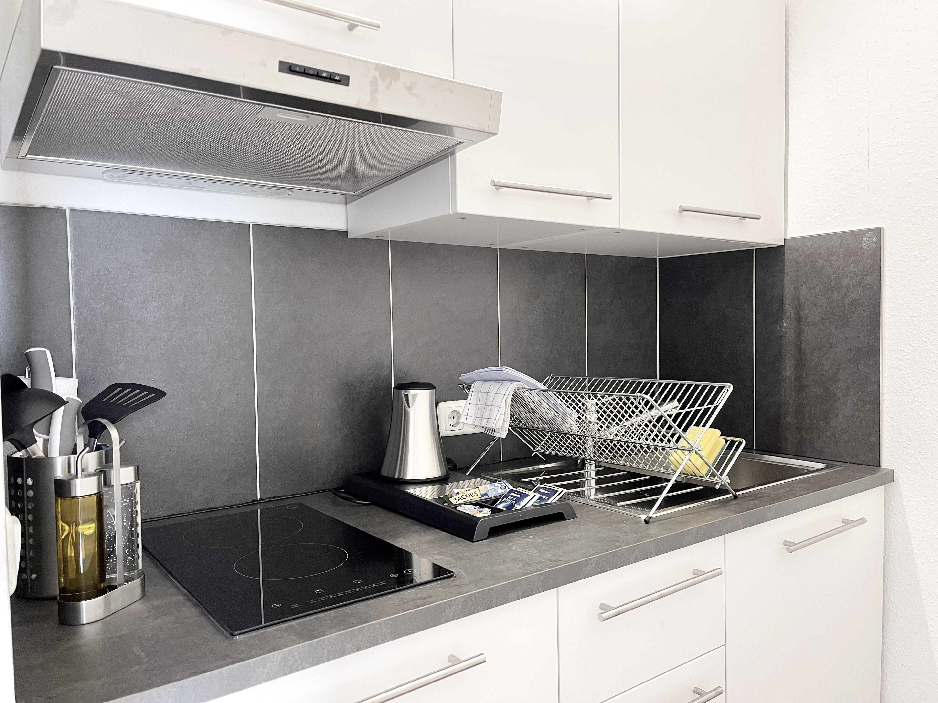 A modern kitchen with a built-in induction cooktop, a kettle, and a drying rack.