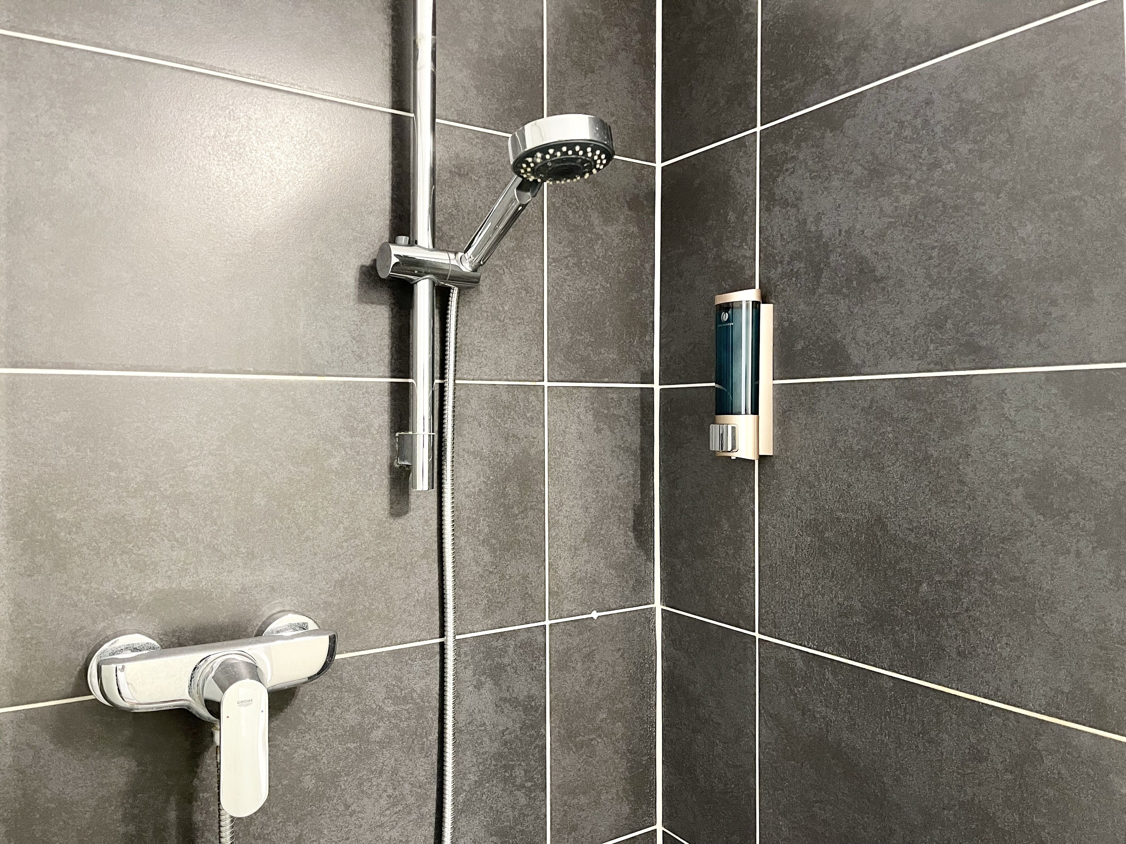 Ein Badezimmer mit Dusche, Duschbrause und Wandseifenspender.
