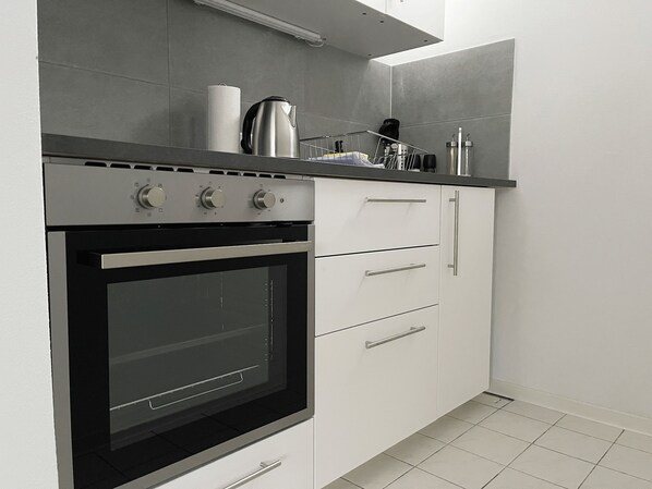 Uma cozinha moderna com forno embutido, armários brancos e bancada de aço inoxidável.