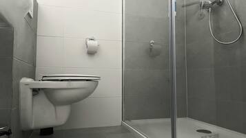 A modern bathroom with a toilet, a shower enclosure, and a toilet paper holder.