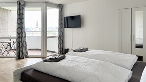 A hotel room with a large bed, a flat-screen TV mounted on the wall, and a balcony with curtains.