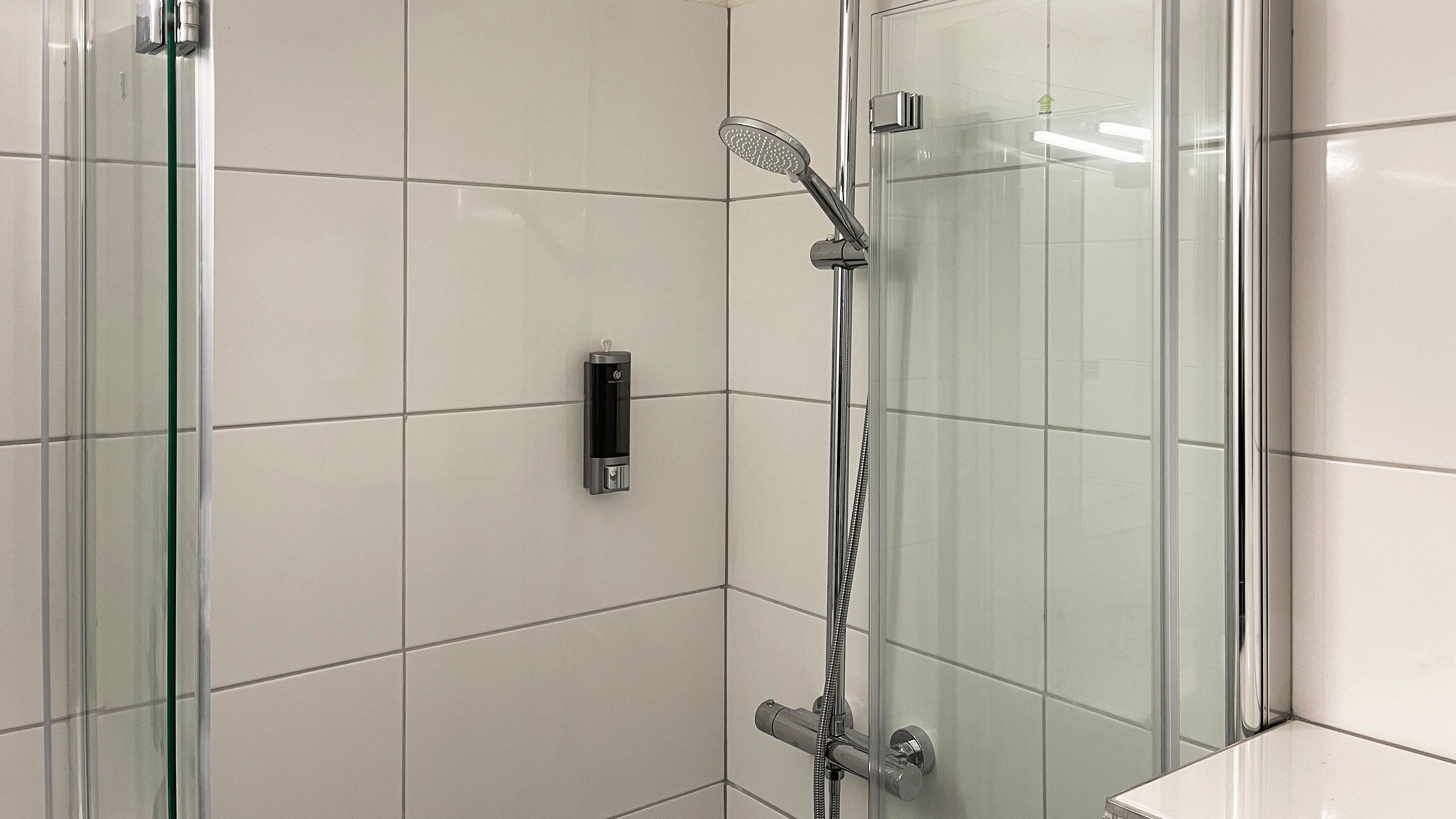 A modern bathroom with a glass shower enclosure, a handheld showerhead, and a wall-mounted control panel.