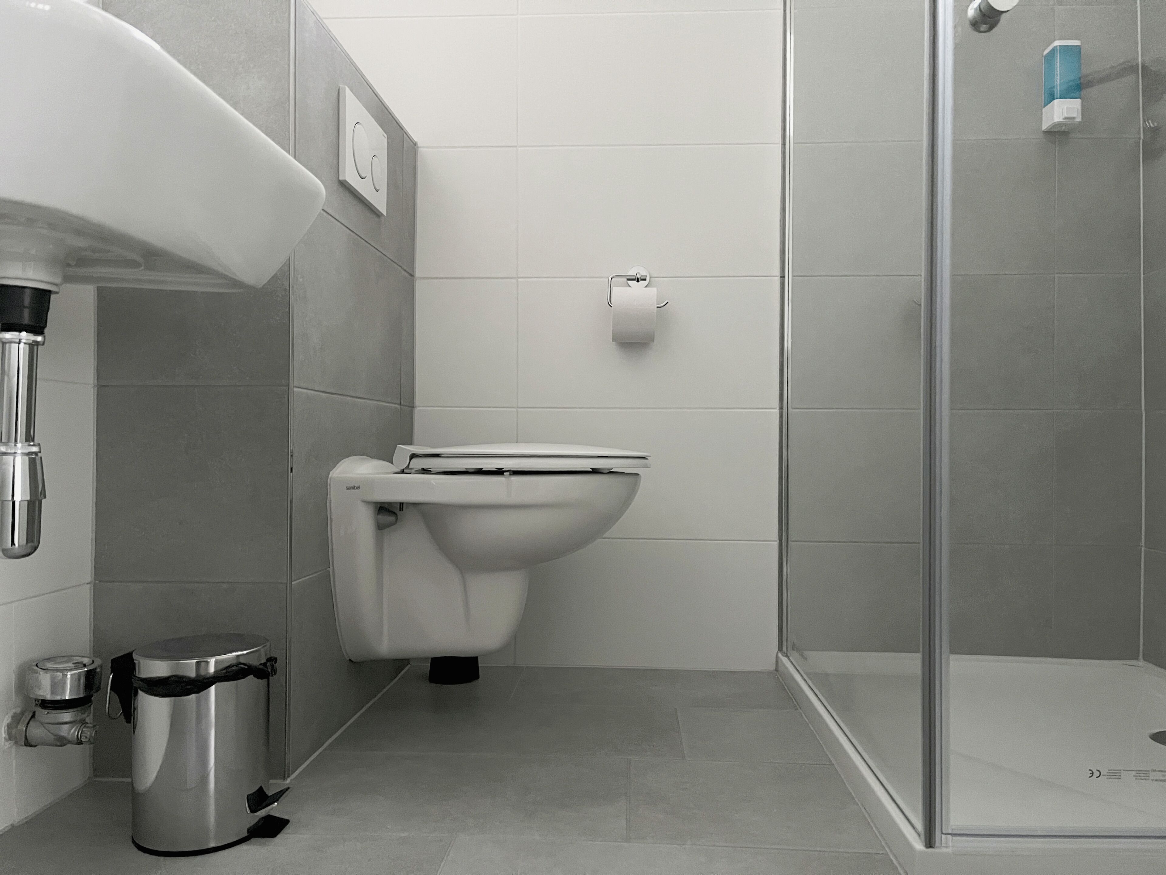 Une salle de bain moderne équipée de toilettes, d’une poubelle et d’un espace douche.