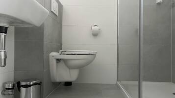 Une salle de bain moderne équipée de toilettes, d’une poubelle et d’un espace douche.