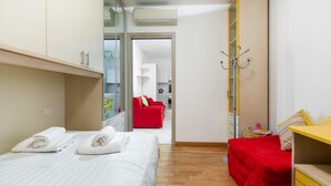 Una habitación de hotel con una cama, un sofá rojo, un aparador amarillo y un perchero.