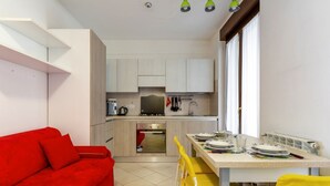 Una cocina compacta con zona de comedor, un sofá rojo y sillas amarillas.