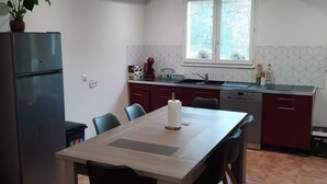 Une cuisine moderne avec un coin repas, comprenant une table en bois, des chaises, un réfrigérateur et une fenêtre donnant sur un paysage verdoyant.