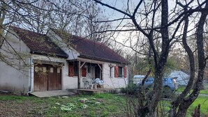 Une maison de plain-pied avec un toit en tuiles, une véranda avec des chaises et un petit jardin fleuri.