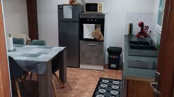 Uma cozinha compacta com geladeira, micro-ondas, forno e pia. Há uma mesa de jantar com cadeiras e um tapete estampado no chão.