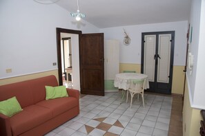 A room with a red sofa, a small table with a white tablecloth, and a door with a decorative item above it.