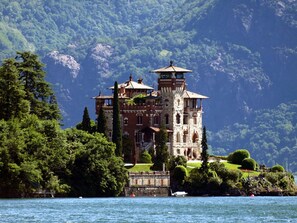 Ein großes, historisches Gebäude mit mehreren Türmen, umgeben von üppiger Vegetation und einem See.