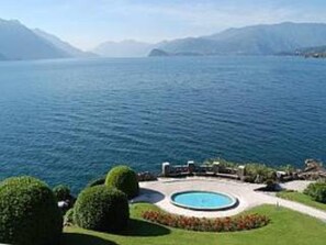 Blick auf einen See mit einem kreisförmigen Pool und einem Gebäude mit einem Garten im Vordergrund.
